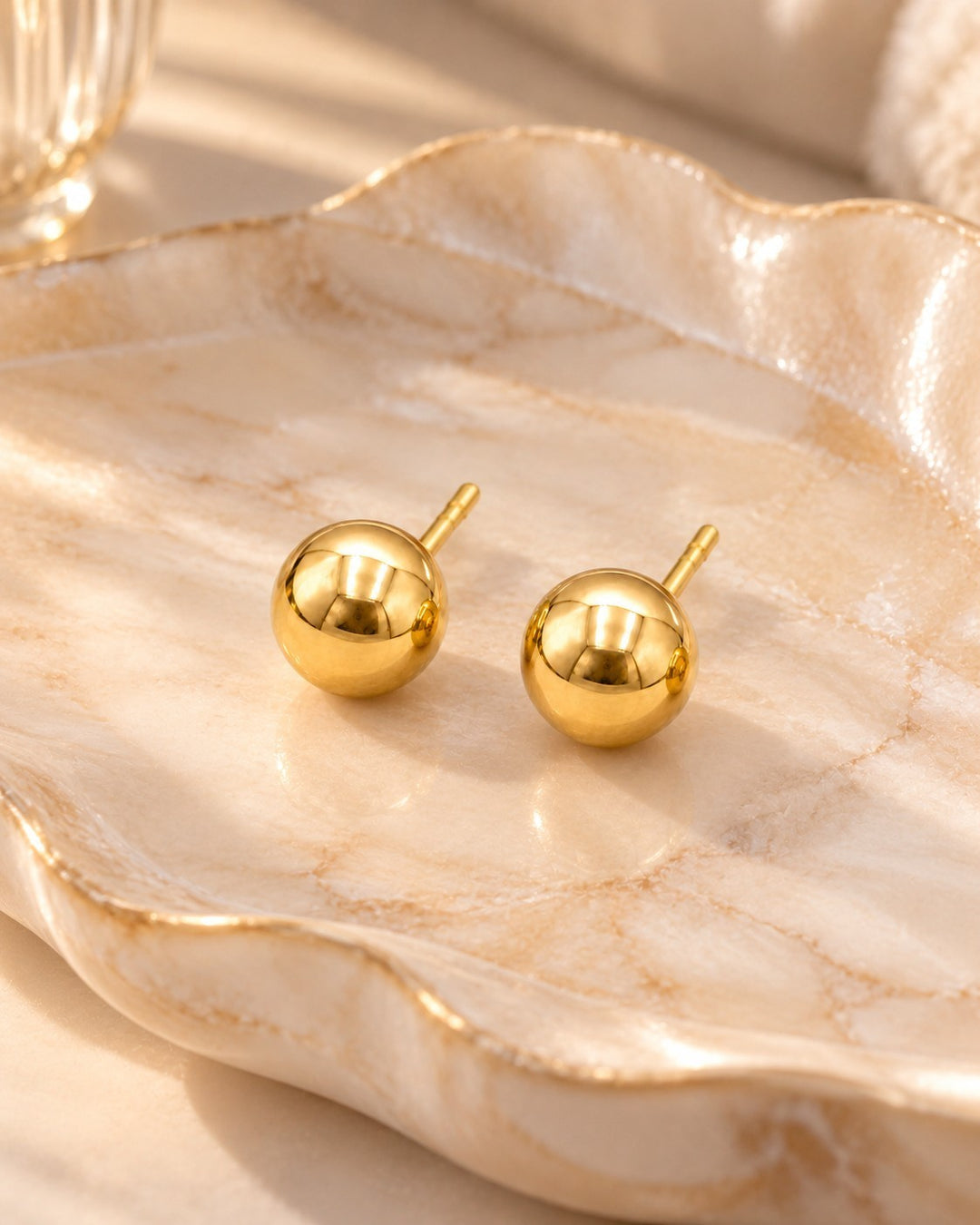 Elli Jewellery 6mm round gold-plated stud earrings with a polished finish resting on a decorative marble dish.