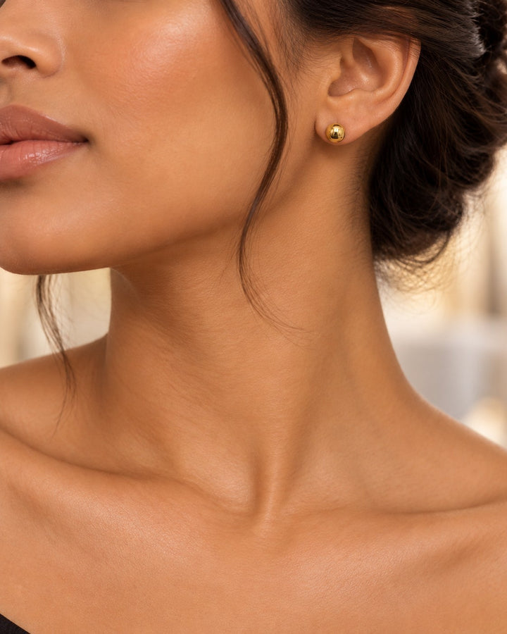 Elli Jewellery 6mm round gold plated stud earrings worn by a woman, featuring a minimalist and waterproof design.