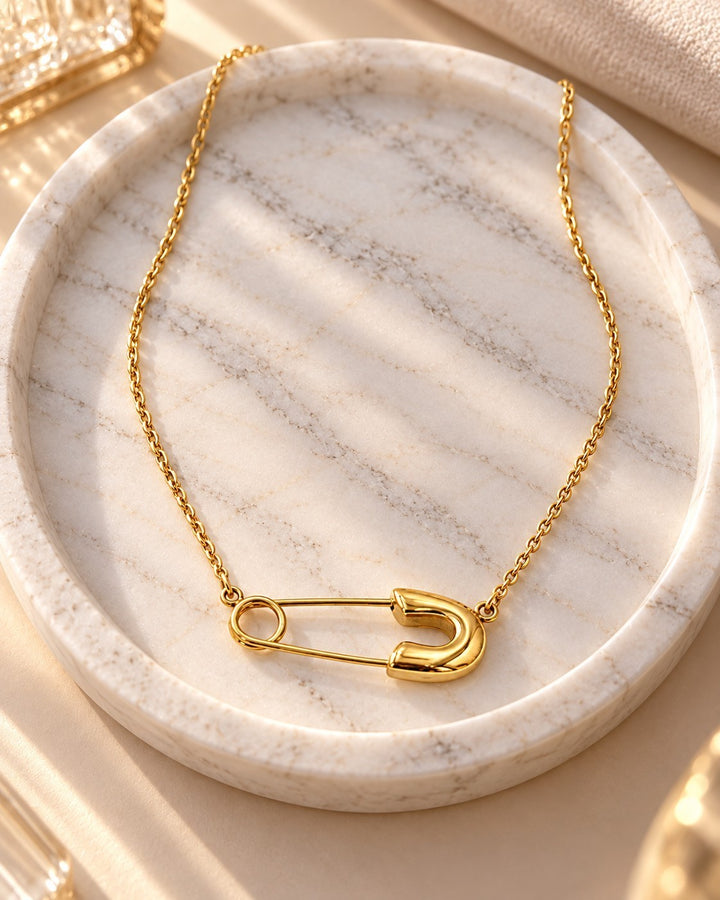 Elli Jewellery gold plated safety pin pendant on a delicate chain resting on a white marble tray.