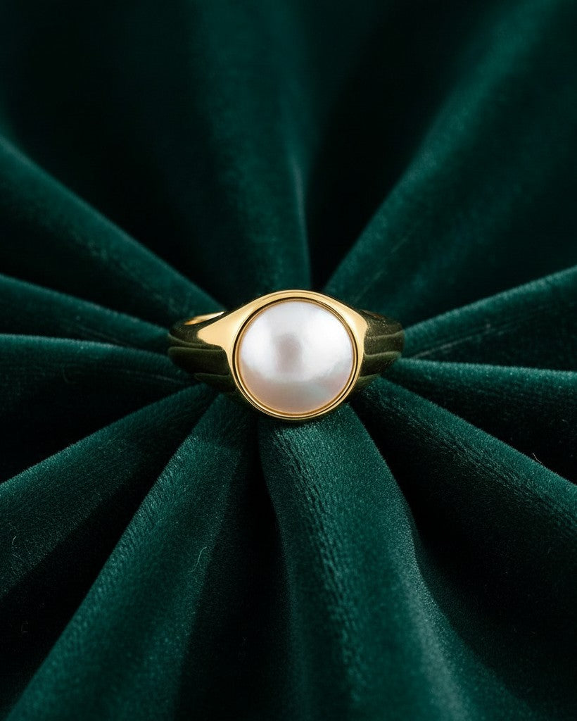 Elli Jewellery gold toned chunky ring featuring a central white pearl-like shell accent on dark green velvet.