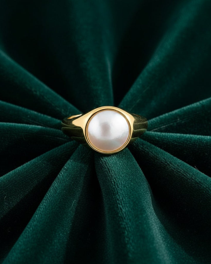 Elli Jewellery gold toned chunky ring featuring a central white pearl-like shell accent on dark green velvet.