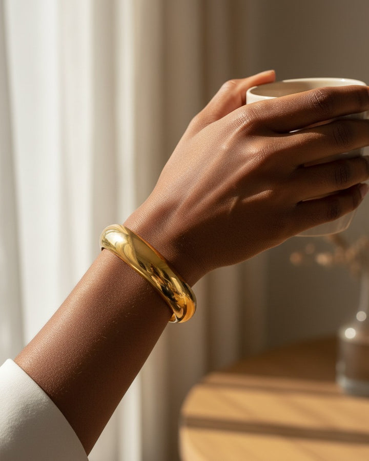 Elli Jewellery gold plated waterproof slim bangle worn on a woman's wrist while holding a coffee cup