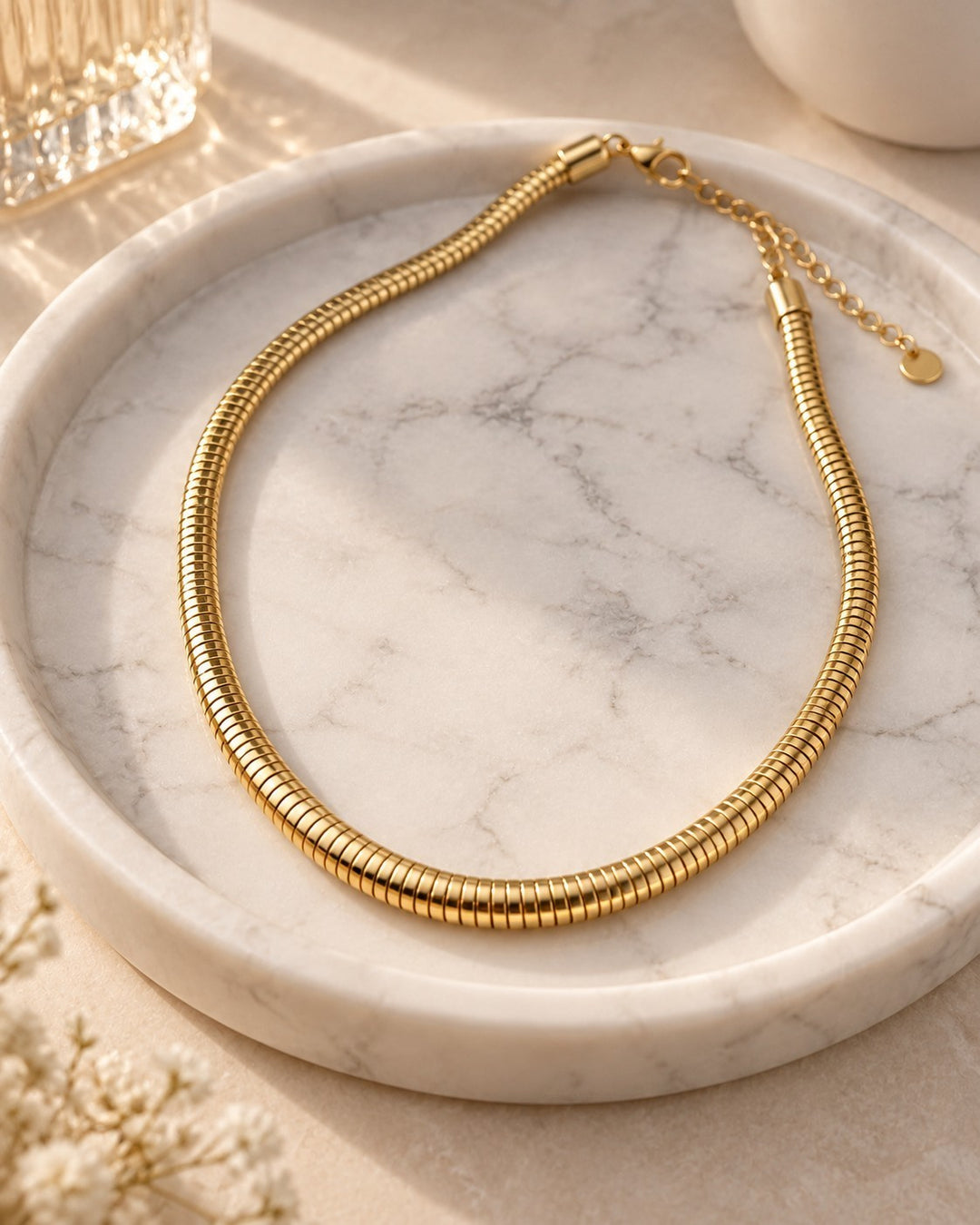 Elli Jewellery gold plated waterproof snake chain necklace with a smooth, sleek finish on a marble tray.