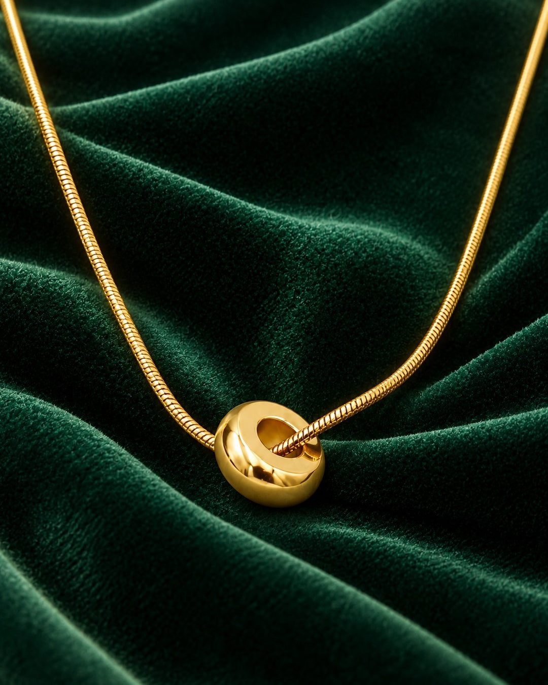 Elli Jewellery gold plated waterproof snake chain necklace with a smooth circular pendant on dark green velvet.