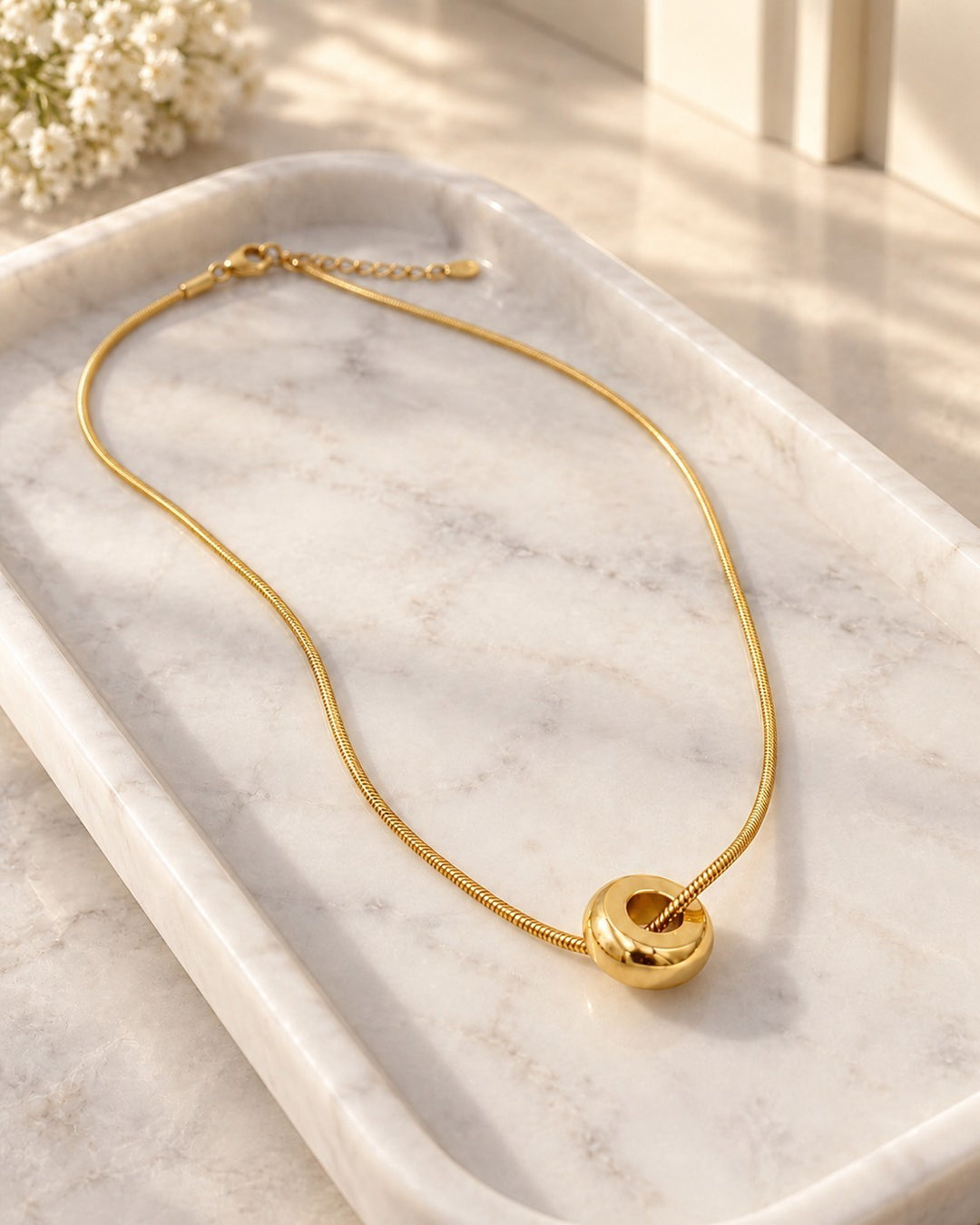 Elli Jewellery gold plated waterproof snake chain necklace with a minimalist round pendant on a marble tray.
