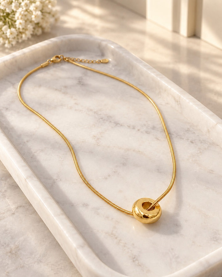 Elli Jewellery gold plated waterproof snake chain necklace with a minimalist round pendant on a marble tray.