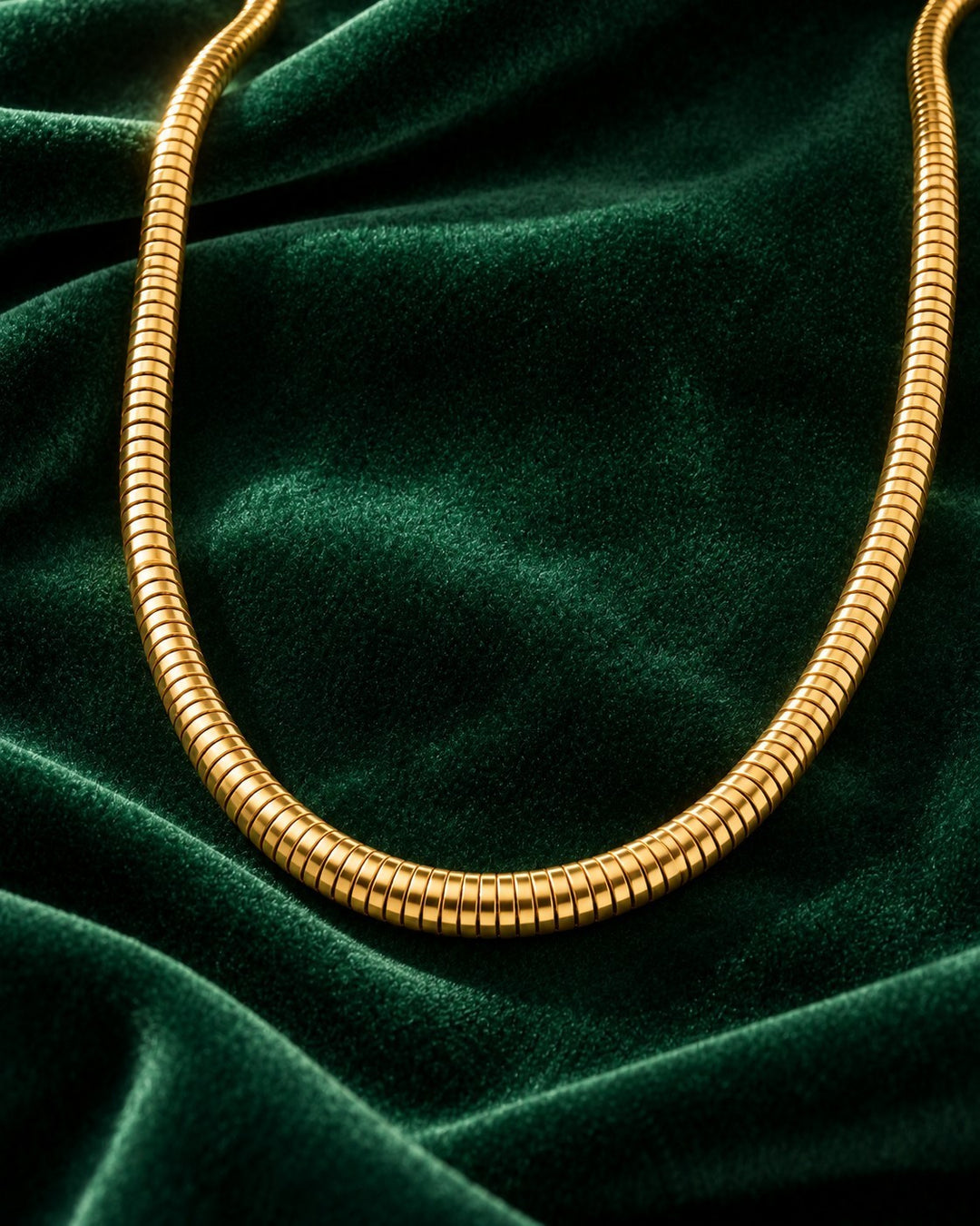 Elli Jewellery gold plated waterproof snake chain necklace resting on a luxurious dark green velvet fabric background.