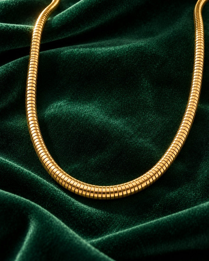 Elli Jewellery gold plated waterproof snake chain necklace resting on a luxurious dark green velvet fabric background.