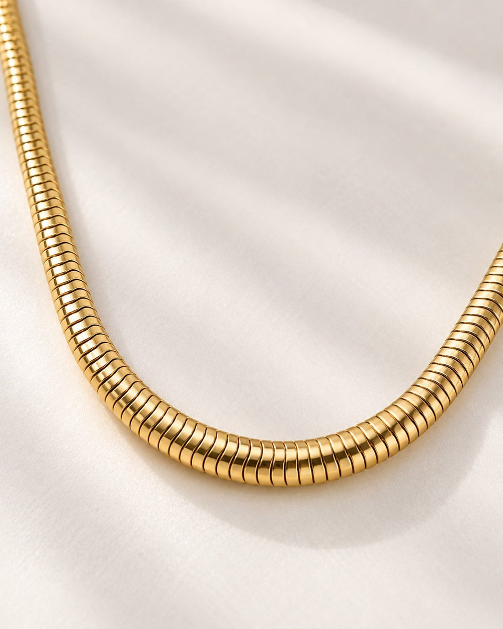 Elli Jewellery gold plated waterproof snake chain necklace with a smooth, sleek finish on a white fabric background.