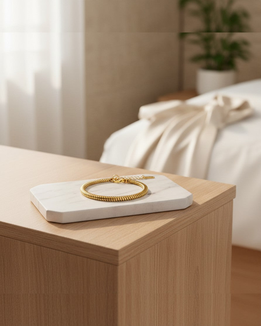 Elli Jewellery 18ct gold plated snake disc chain bracelet resting on a white marble tray in a bright bedroom setting.
