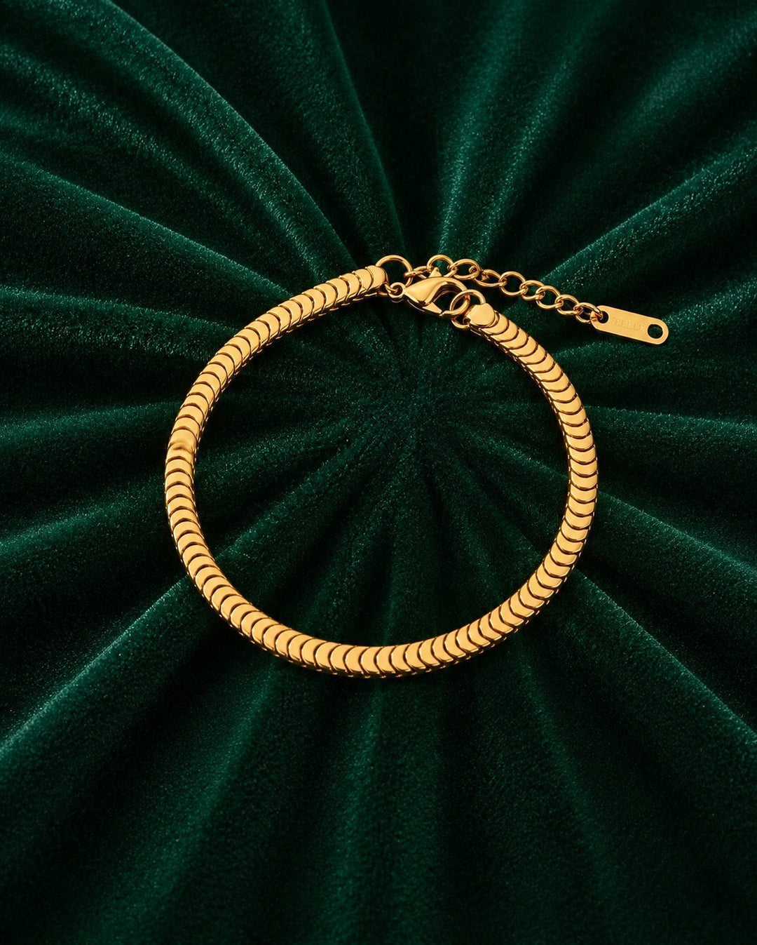Elli Jewellery gold plated snake disc chain bracelet with an adjustable extender on a dark green velvet background.
