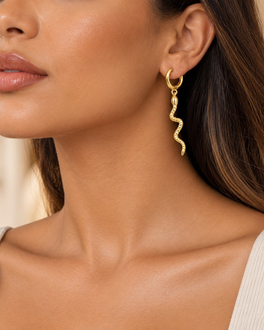 Elli Jewellery gold plated snake texture huggie hoop earrings worn by a woman, featuring a dangling snake charm.
