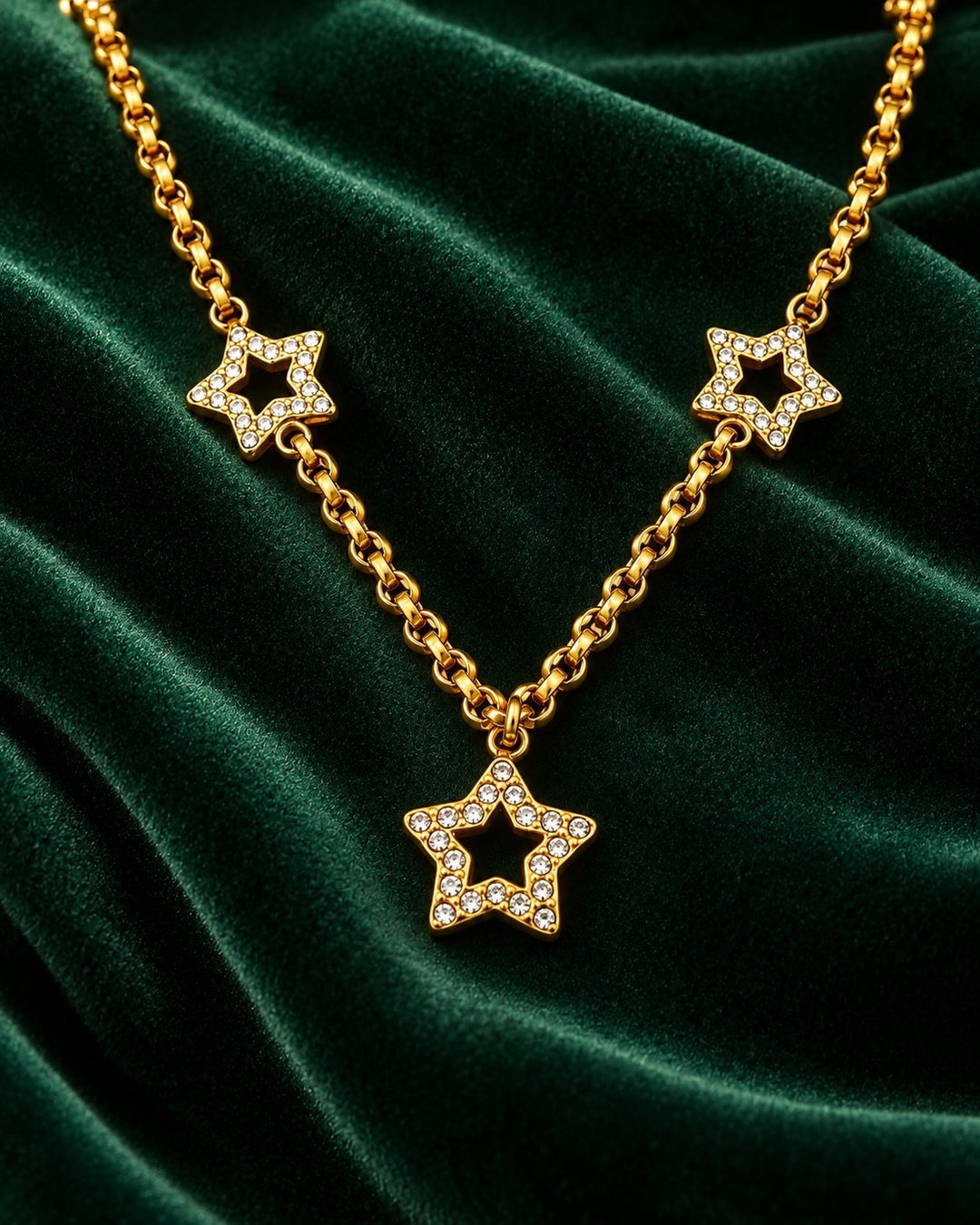 Elli Jewellery gold plated celestial star necklace with crystal accents on a dark green velvet background