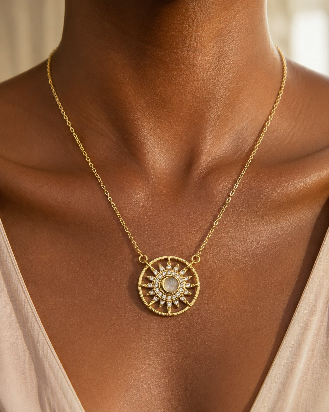 Elli Jewellery gold plated starburst medallion necklace with a cream cabochon and crystal rays worn on a model