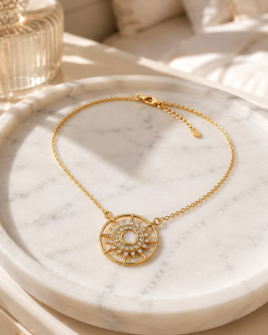 Elli Jewellery gold plated starburst medallion necklace with a cream cabochon and crystal rays on a marble tray