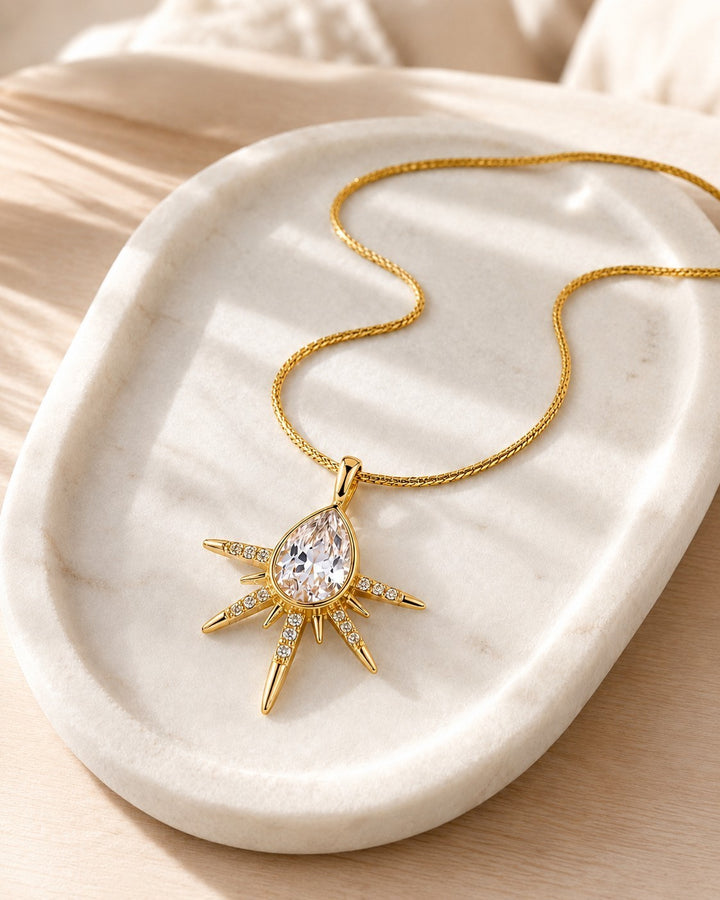 Elli Jewellery gold plated starburst pendant necklace with a central pear-shaped crystal on a fine snake chain.
