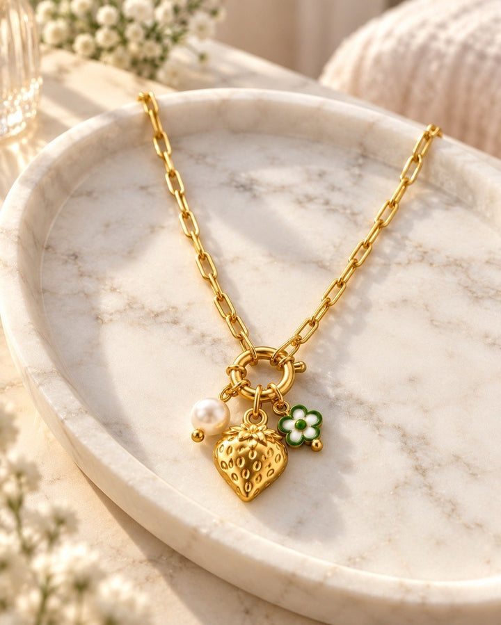 Elli Jewellery gold plated chain necklace featuring a strawberry, pearl, and flower charm on a marble tray.