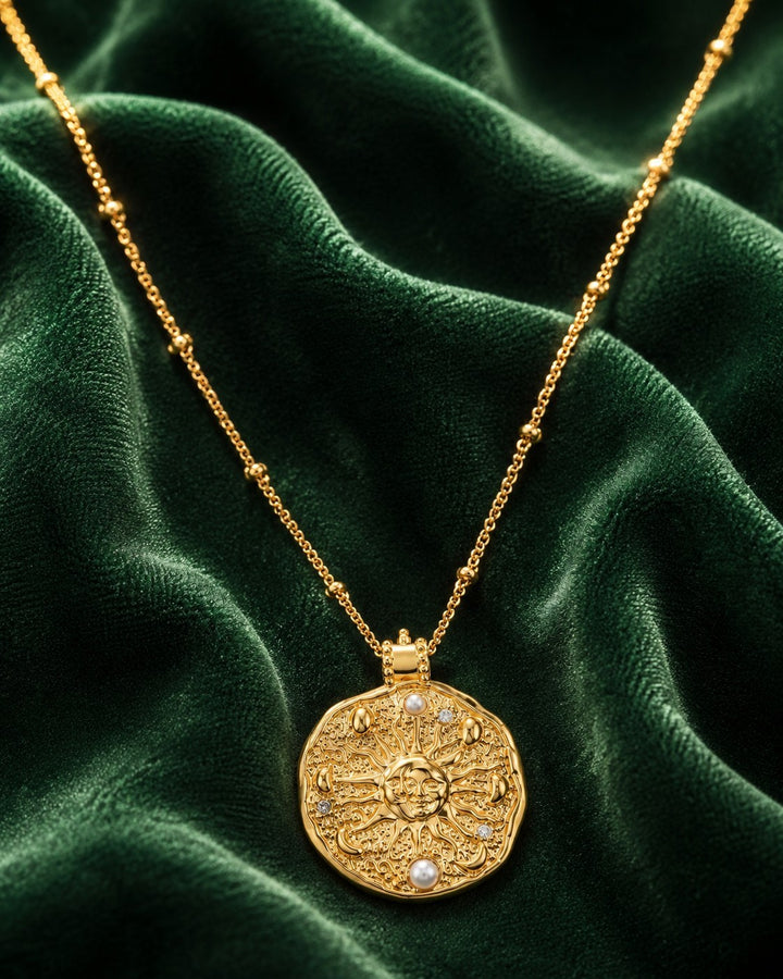 Elli Jewellery gold plated sun medallion necklace with pearl accents and station chain on dark green velvet fabric