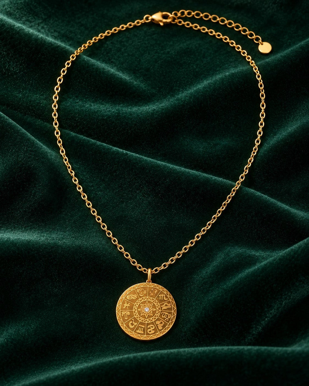 Elli Jewellery gold plated celestial sundial coin pendant necklace on a dark green velvet background.