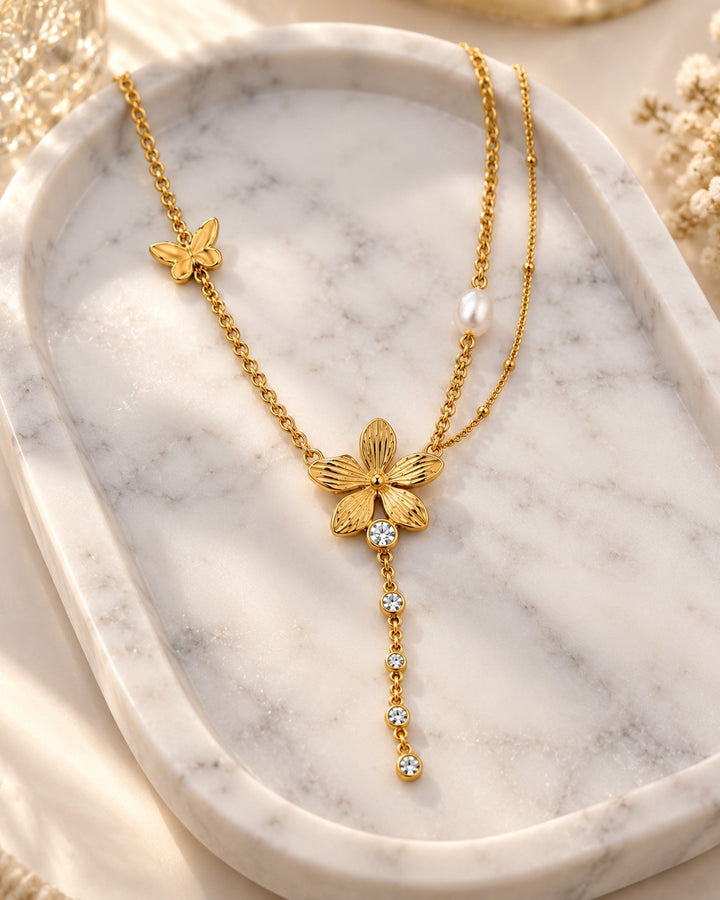 Elli Jewellery gold plated sunflower charm necklace with a butterfly, pearl accent, and crystal drop on a marble tray