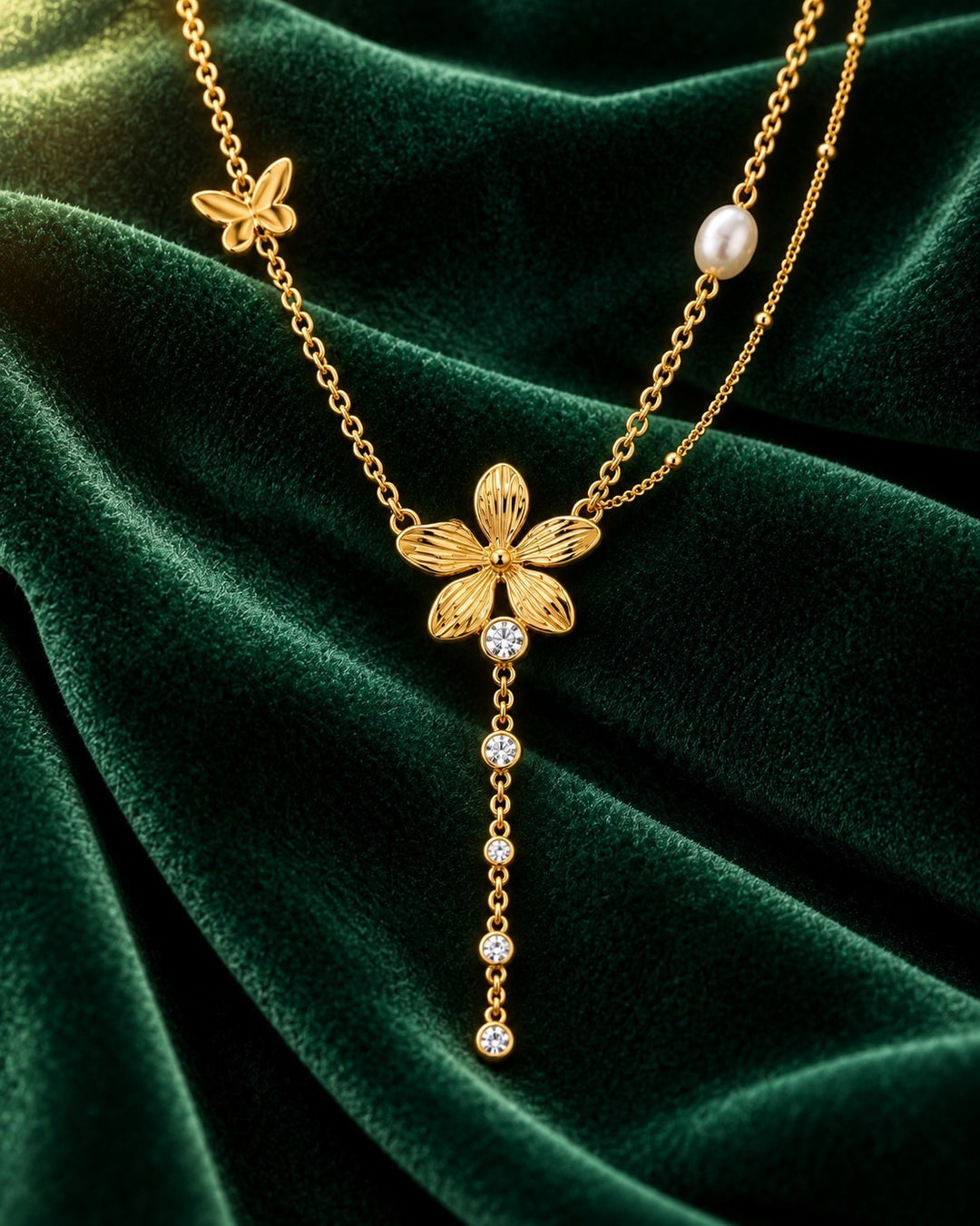 Elli Jewellery gold plated sunflower charm necklace with a butterfly, pearl, and crystal drop on green velvet.