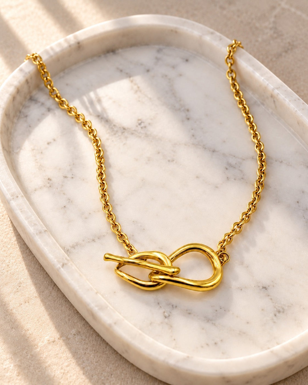 Elli Jewellery gold plated minimalist T-bar cross pendant necklace resting on a white marble tray