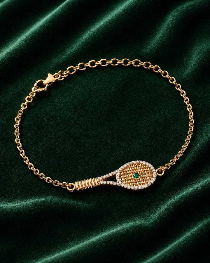 Elli Jewellery gold plated tennis racquet charm bracelet with pavé crystals and a green crystal ball on green velvet.
