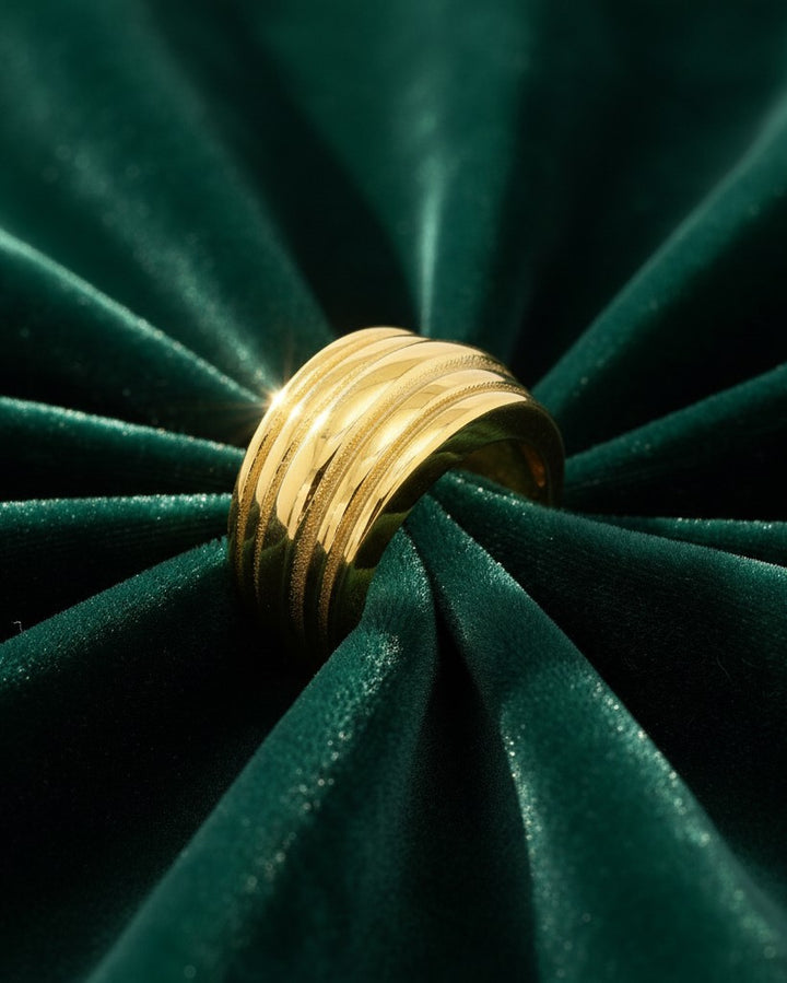 Elli Jewellery gold plated minimalist band ring with textured linear details on a dark green velvet background.