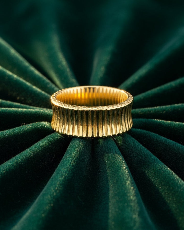 Elli Jewellery gold plated inverse band ring with a textured, ribbed finish resting on dark green velvet.