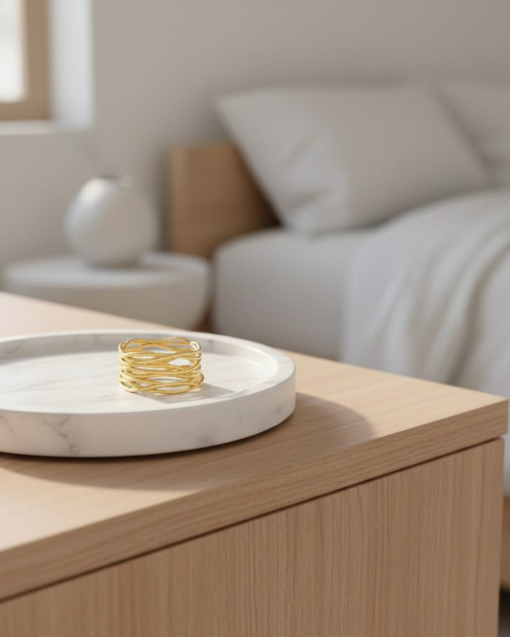 Elli Jewellery wide gold plated band ring with an intricate textured reed pattern resting on a marble tray.