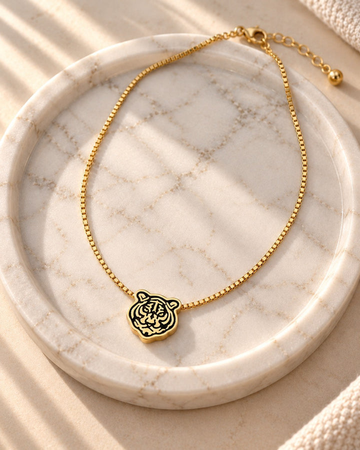 Elli Jewellery gold plated tiger face pendant necklace on a delicate box chain resting on a marble tray