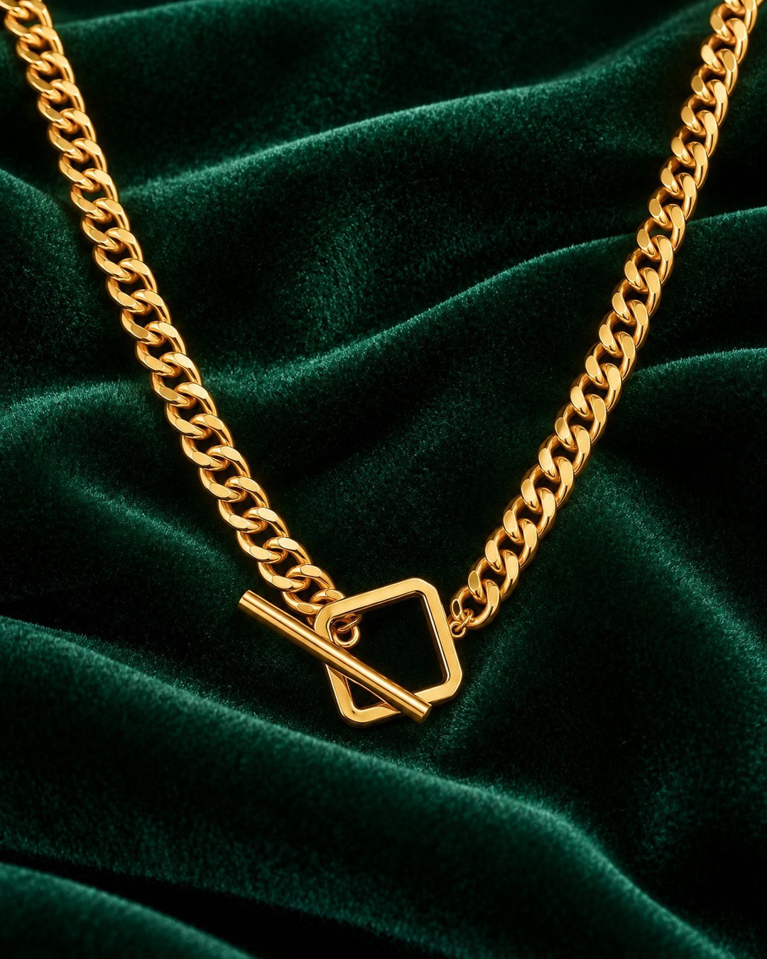 Elli Jewellery gold plated curb chain necklace with a square toggle clasp resting on dark green velvet fabric.