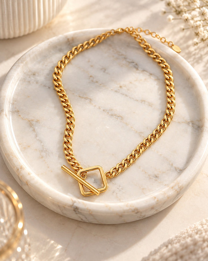 Elli Jewellery gold plated curb chain necklace with a square toggle clasp resting on a white marble tray.