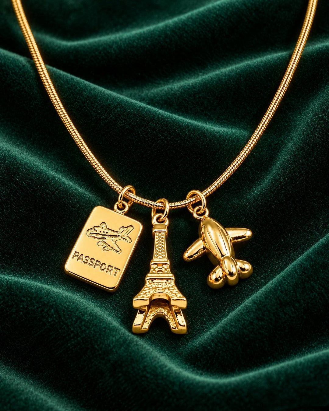 Elli Jewellery gold plated necklace featuring Eiffel Tower, passport, and airplane charms on a green velvet background.