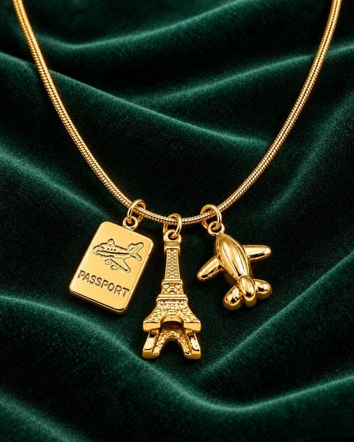 Elli Jewellery gold plated necklace featuring Eiffel Tower, passport, and airplane charms on a green velvet background.