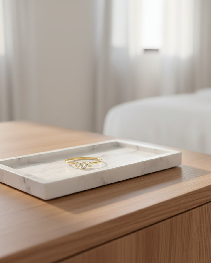 Elli Jewellery gold plated trilogy ring with three sparkling cubic zirconia stones resting on a white marble tray.