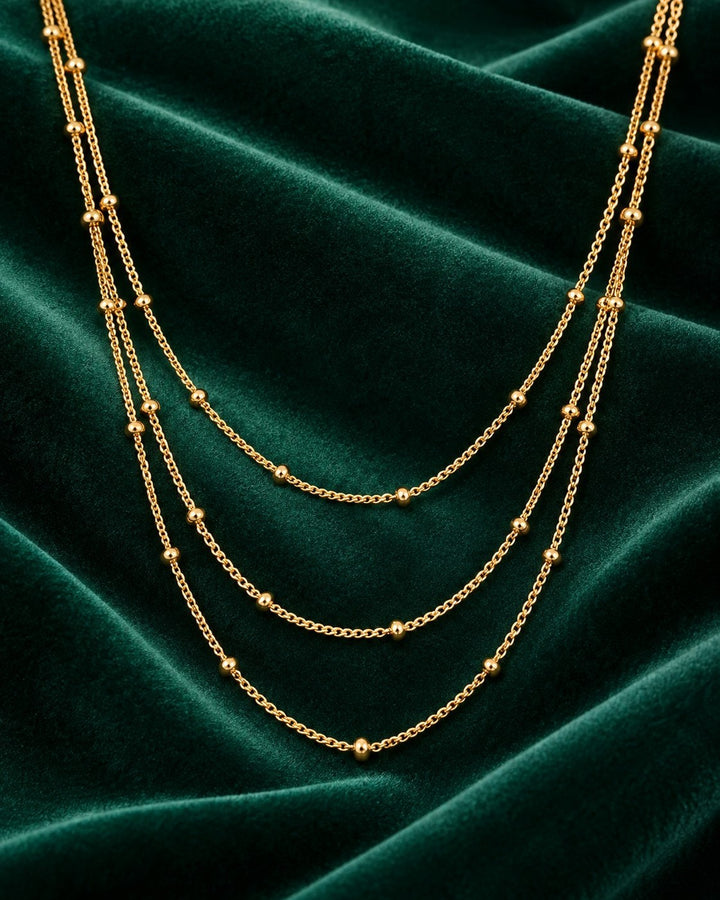 Elli Jewellery gold plated triple layered chain necklace with delicate beads on a dark green velvet background