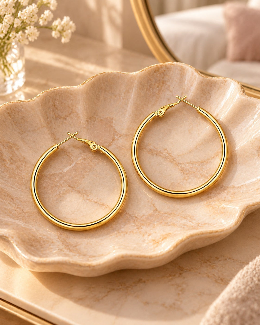 Elli Jewellery gold plated tube hoop earrings with a smooth polished finish resting on a decorative shell dish