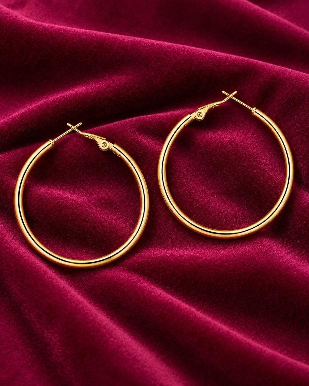 Elli Jewellery 18ct gold plated brass tube hoop earrings with a polished finish on a deep red velvet background