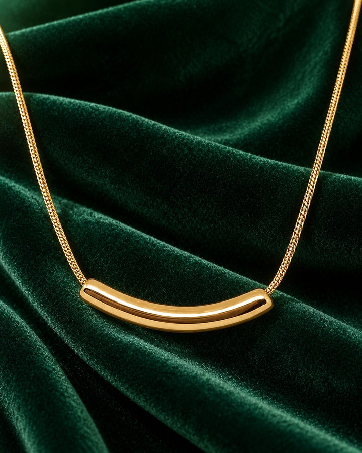 Elli Jewellery gold plated snake chain necklace with a sleek, sculptural tusk pendant on a dark green velvet background