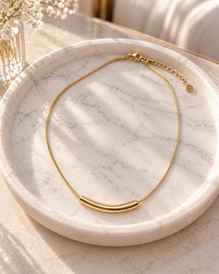 Elli Jewellery gold plated snake chain necklace with a curved tusk pendant resting on a white marble tray.