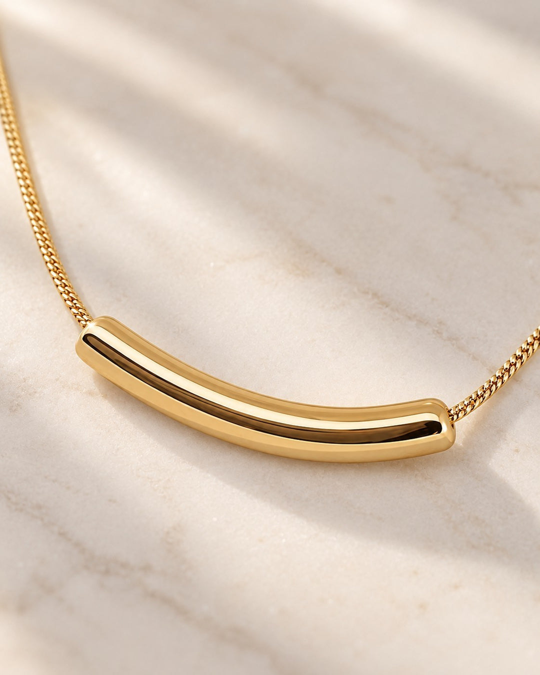 Elli Jewellery gold plated snake chain necklace with a sleek, sculptural tusk pendant on a marble surface.