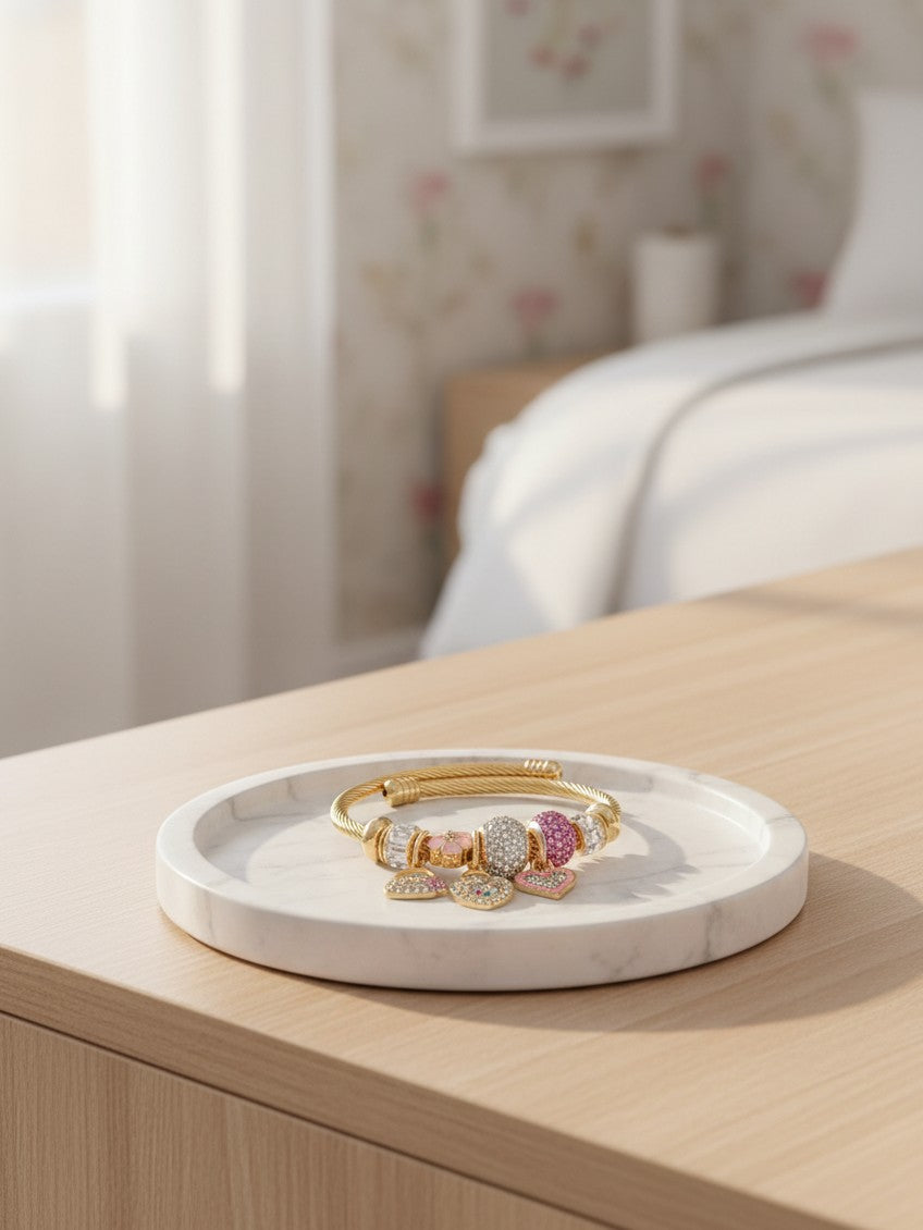 Elli Jewellery gold plated twisted cuff bracelet with pink and crystal beads and dangling heart charms on a tray.
