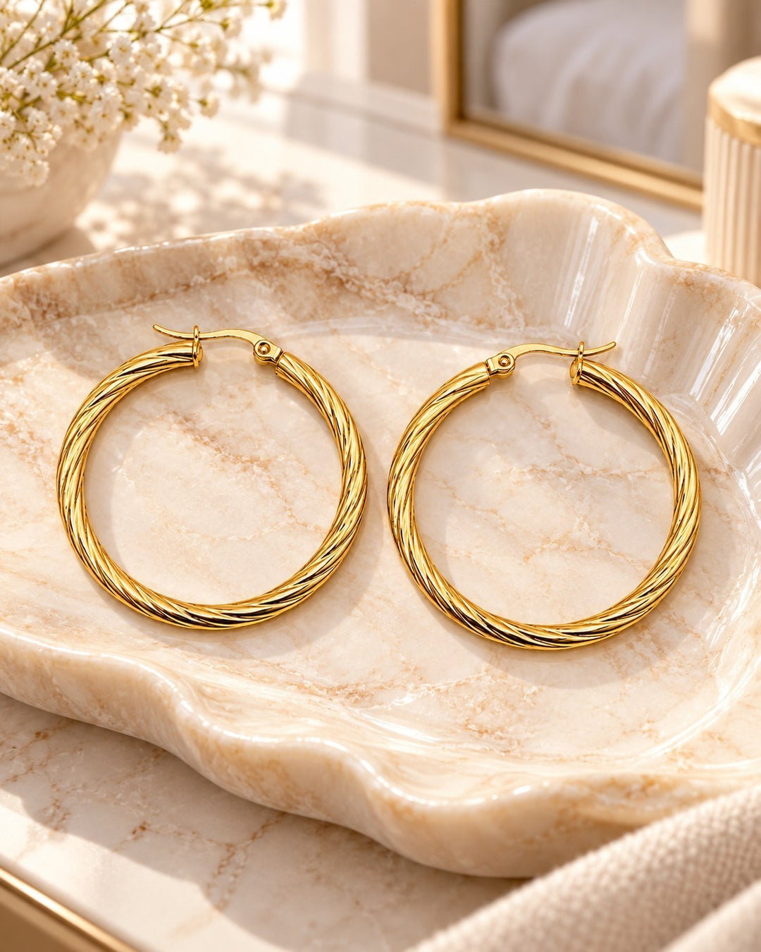 Elli Jewellery 41mm gold-plated twisted hoop earrings resting on a decorative marble shell dish.