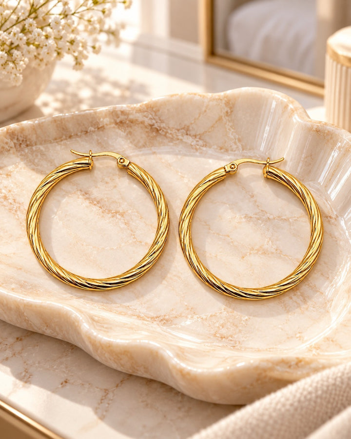 Elli Jewellery 41mm gold-plated twisted hoop earrings resting on a decorative marble shell dish.