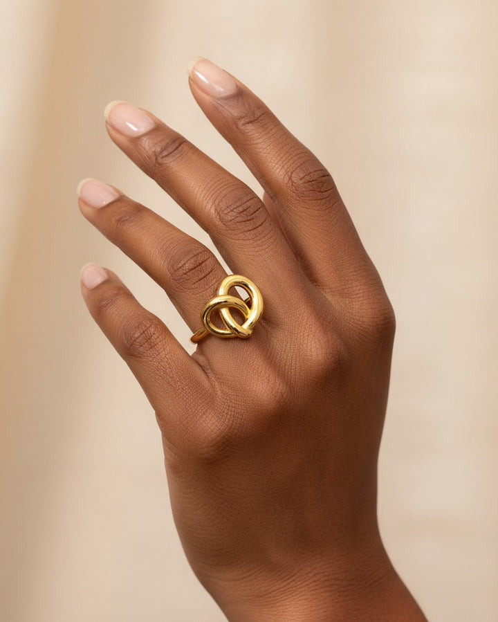 Elli Jewellery gold plated twisted knot statement ring worn on a finger, featuring a sculptural interwoven design.