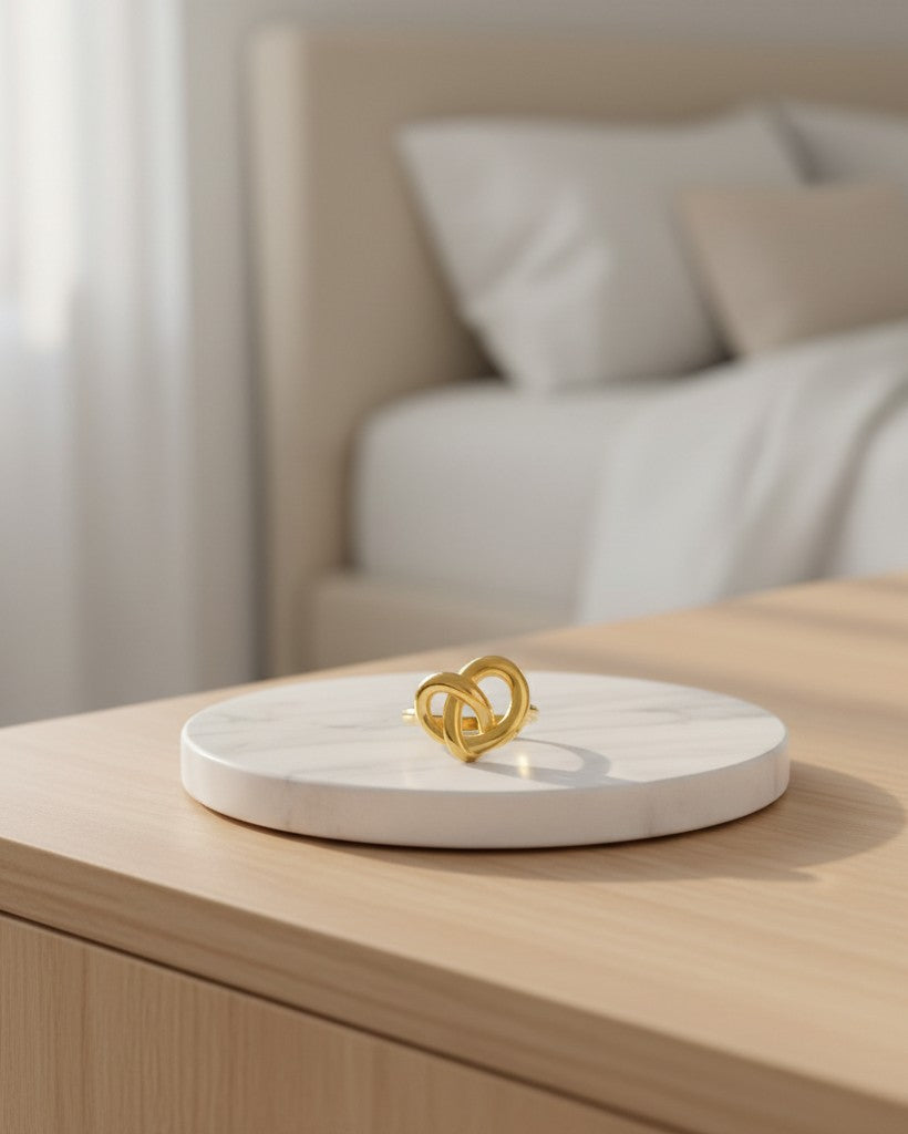 Elli Jewellery gold plated twisted knot statement ring resting on a white marble display stand in a bedroom setting.