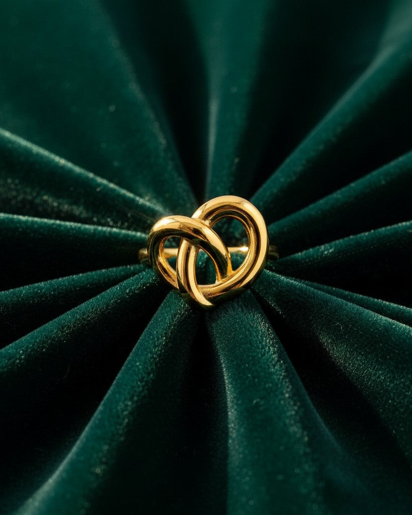 Elli Jewellery gold plated twisted knot statement ring resting on a dark green velvet background