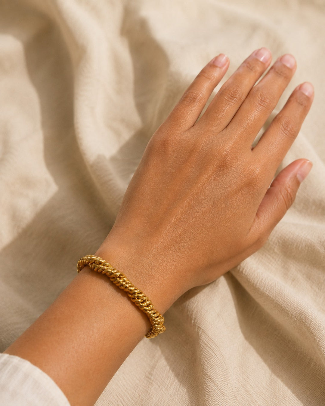 Elli Jewellery gold plated twisted rope chain bracelet worn on a wrist against a neutral linen background