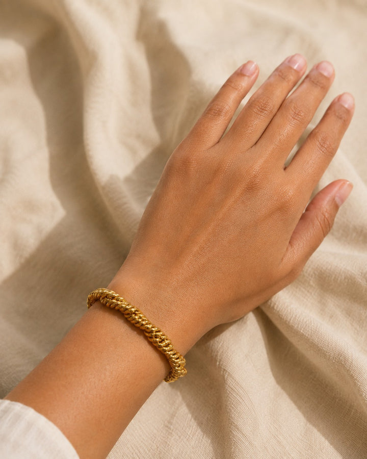 Elli Jewellery gold plated twisted rope chain bracelet worn on a wrist against a neutral linen background